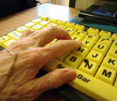 A hand with varicose veins rests on an a high contrast accessible computer keybard